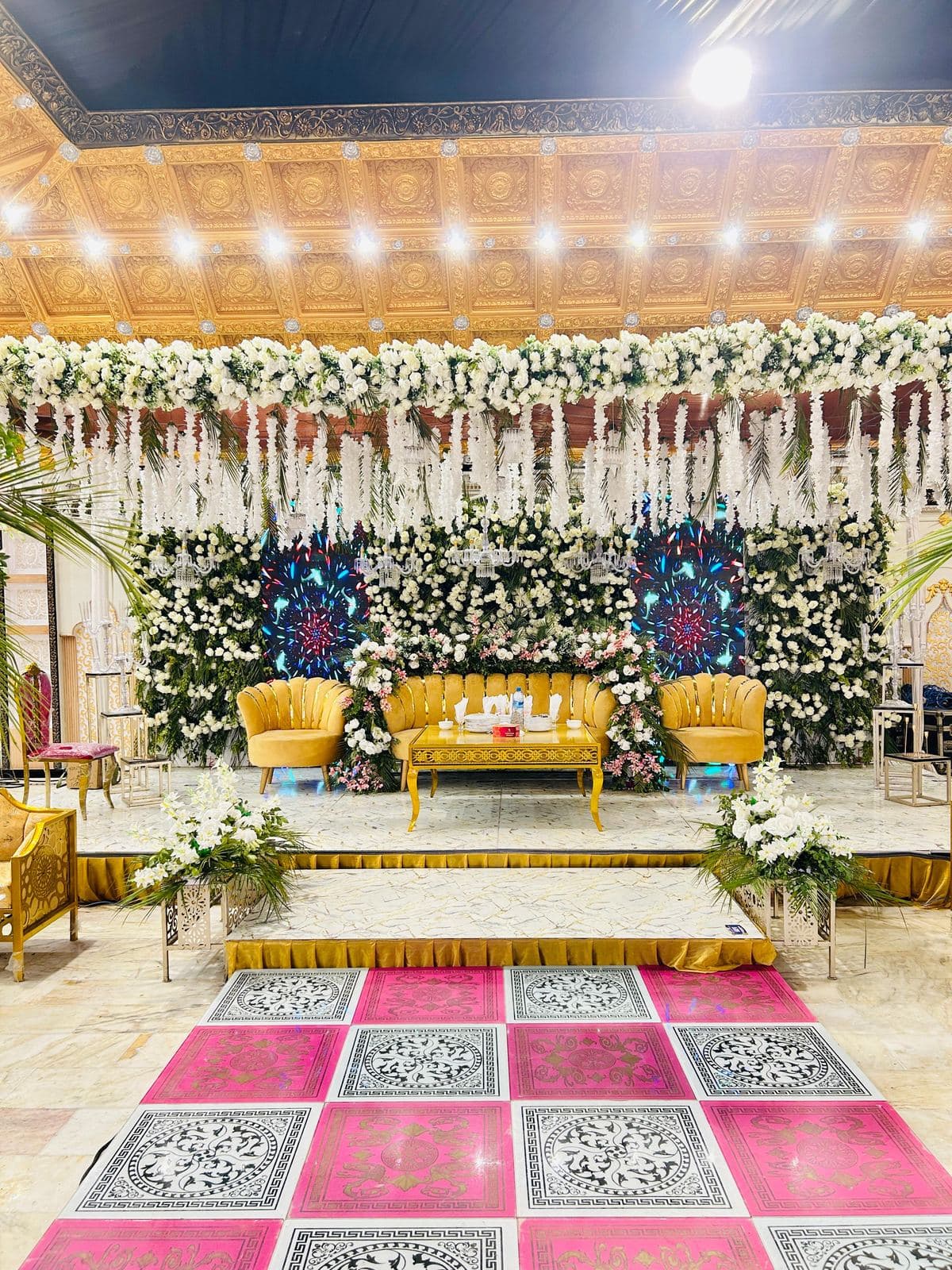 Wedding stage with gold sofas, a white floral canopy and a patterned floor